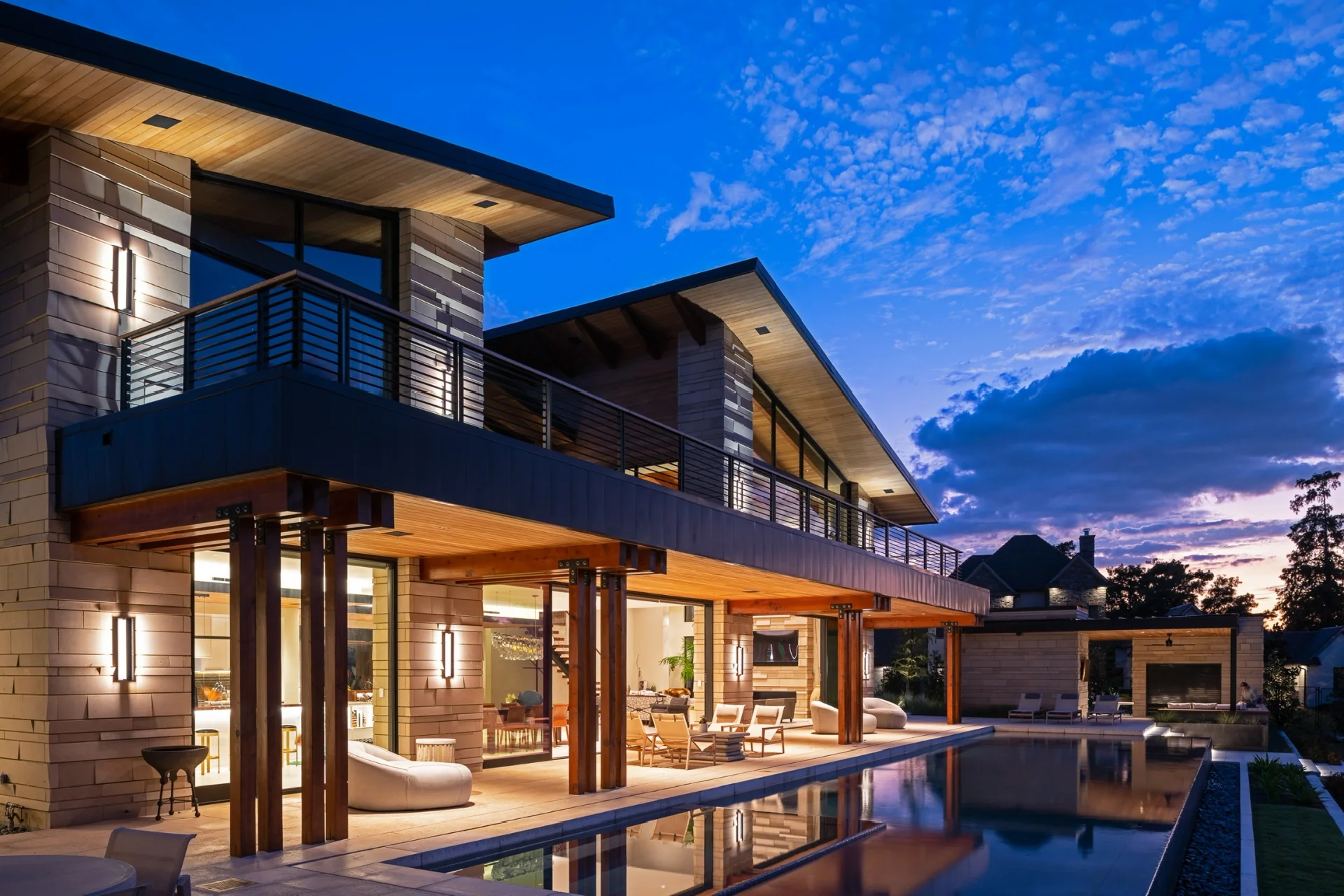 Una residencia terminada de Winn Wittman al anochecer — volúmenes modernos, aleros profundos y un salón principal de vidrio sobre un estanque reflectante.